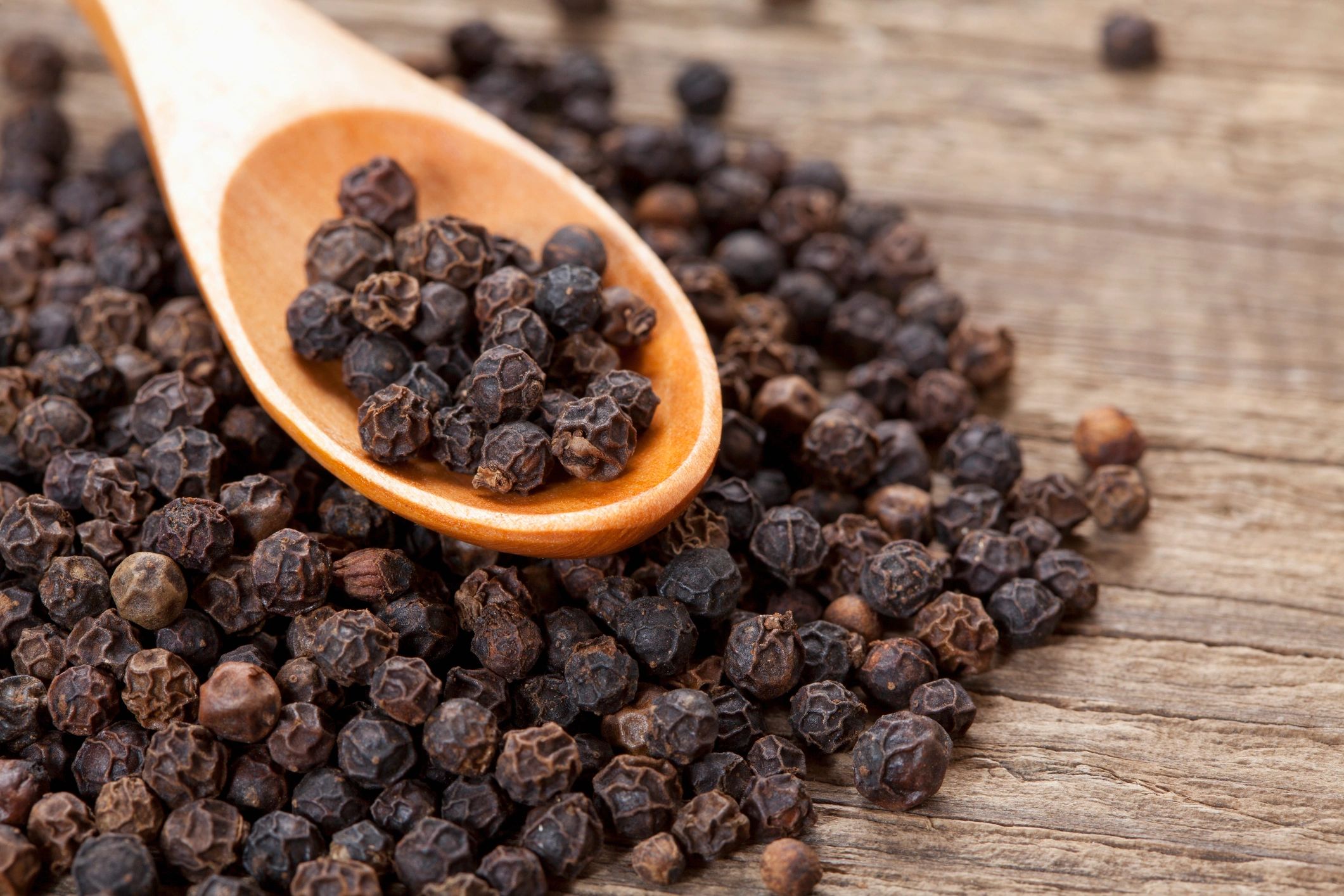 Black peppercorns in a wooden spoon